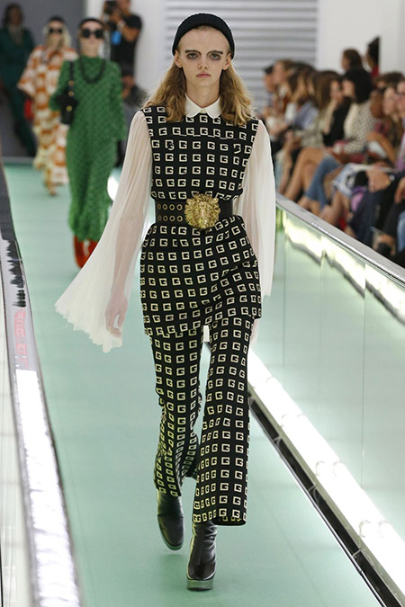 No desfile da Gucci da MFW Primavera / Verão 20, modelo veste conjunto em preto com o G da marca em branco e camisa de manga longa e esvoaçante.
