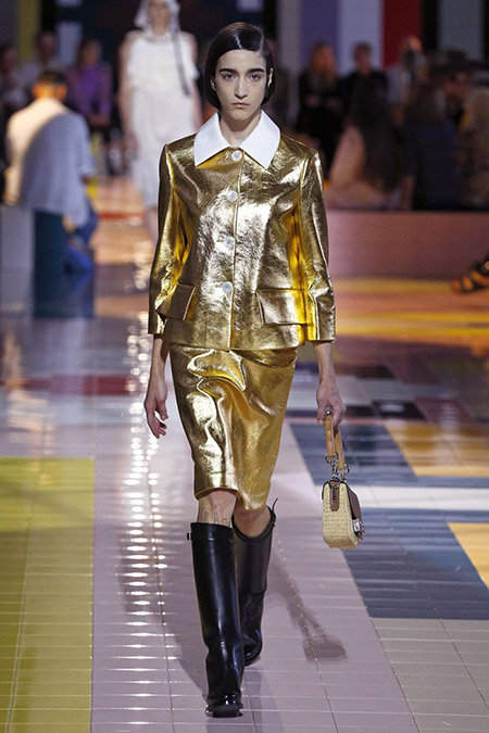 No desfile da Prada da MFW Primavera / Verão 20, modelo veste taieur dourado metálico e botas cano alto pretas.