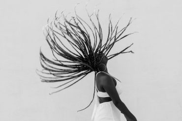 Mulher preta joga as tranças para trás, num gesto forte de resgate da ancestralidade africana.