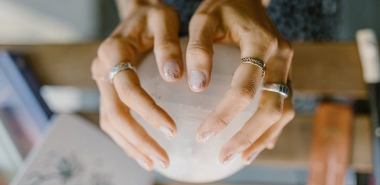 ma~e de mulher branca com aneis segurando uma bola de cristal